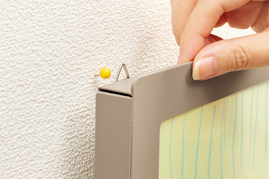 「三角吊りカン」部分にフォーカスしている画像。壁に細いピンが刺さっていて、そこに三角吊りカンを引っかけようとしている様子。