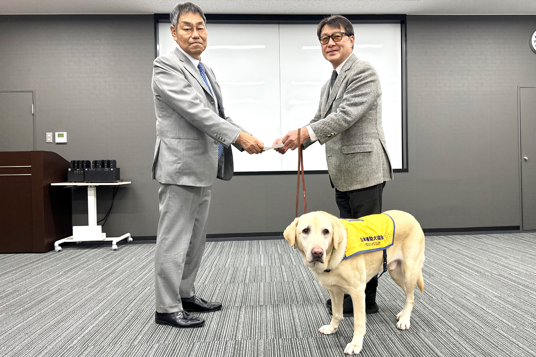 弊社社長の髙橋が元盲導犬のルーカス君（ラブラドールレトリバー）を「心のバリアフリー大使」に任命しているところ。